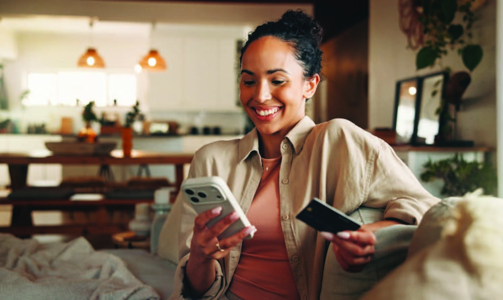 A woman sitting on her couch paying on cell phone with credit card